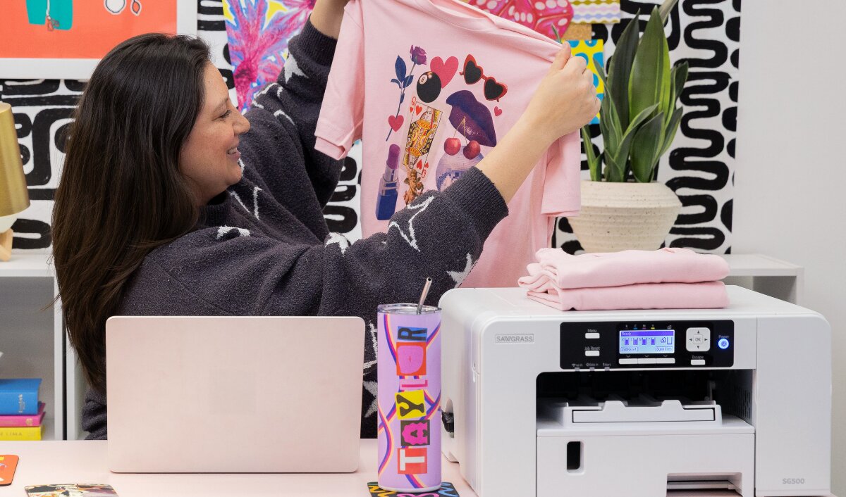 A creator displaying a custom shirt beside a Sawgrass VersiFlex printer