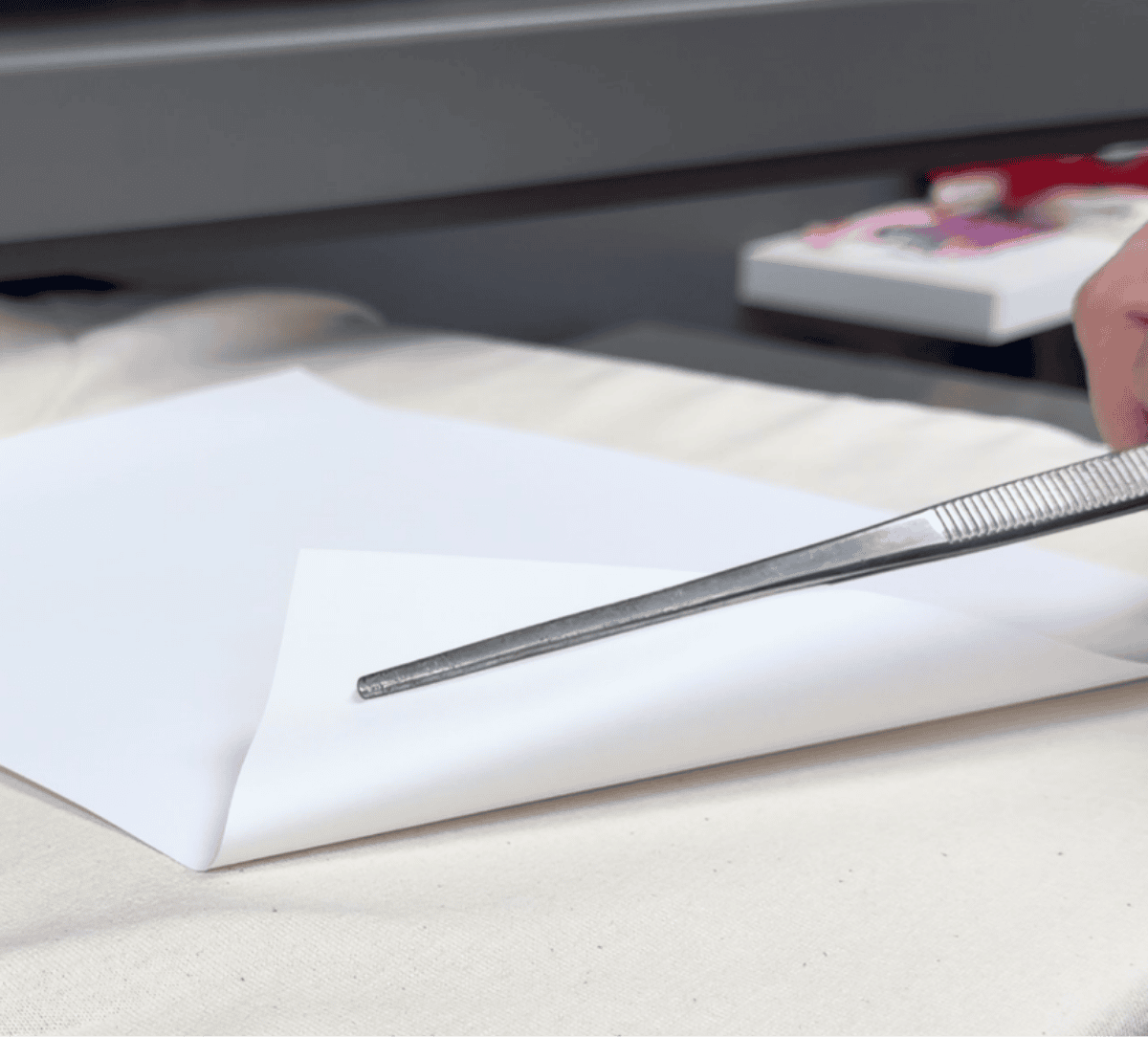 Tweezers lifting a corner of transfer paper